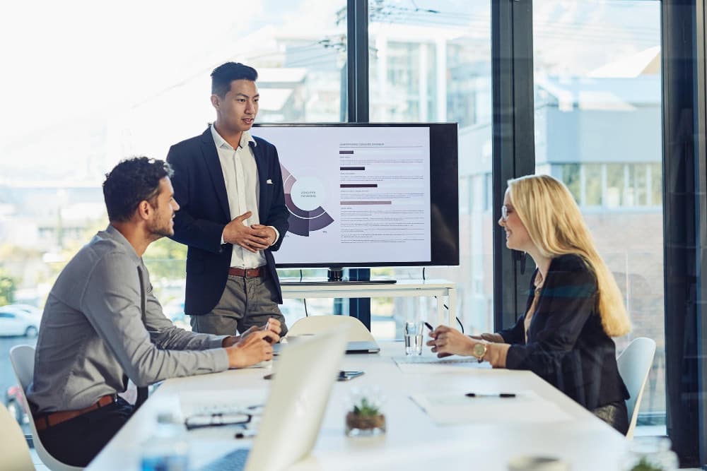 Team commerciale B2B in riunione con dashboard CRM aziendale a parete: presentazione di pipeline vendite, schede cliente e analisi dati in una sala riunioni moderna