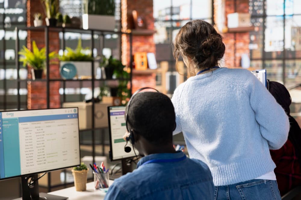 Responsabile che supervisiona due collaboratori mentre usano un software gestionale su monitor in ufficio — visualizzazione di sistemi aziendali a confronto: CRM, gestionale ed ERP