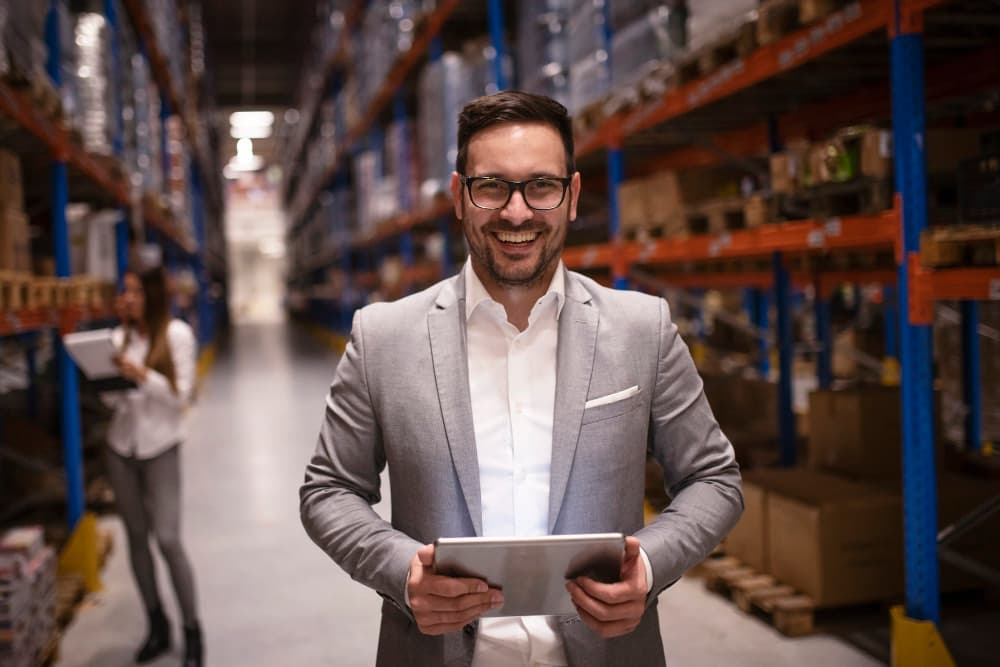 Account manager B2B sorridente con tablet in un magazzino: il CRM post vendita supporta customer success e gestione clienti sul campo