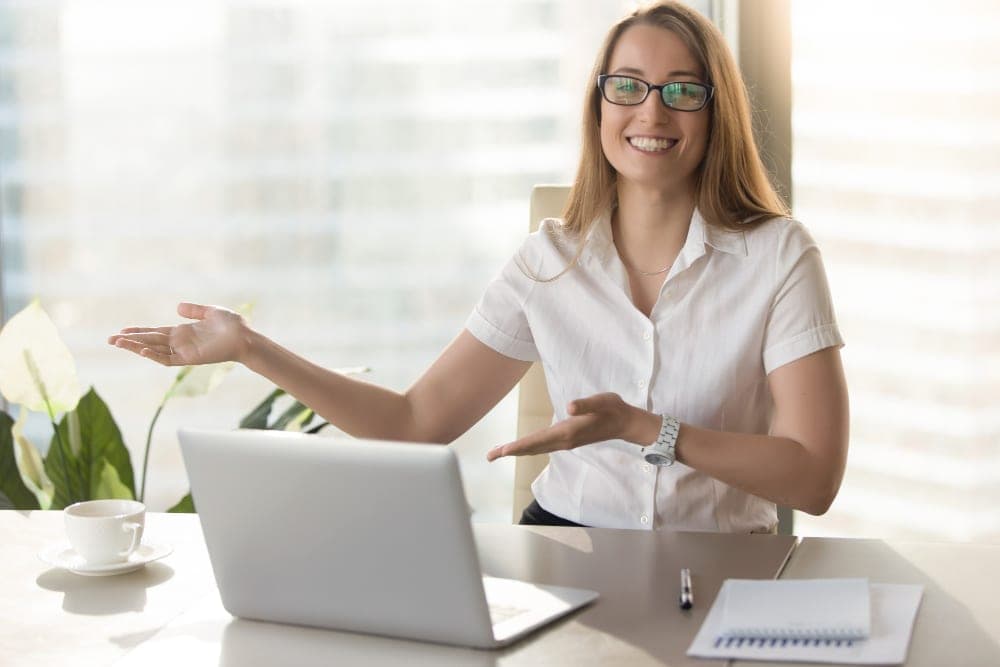 Psicologa sorridente alla scrivania mentre presenta i contenuti del proprio profilo social con un gesto aperto di benvenuto